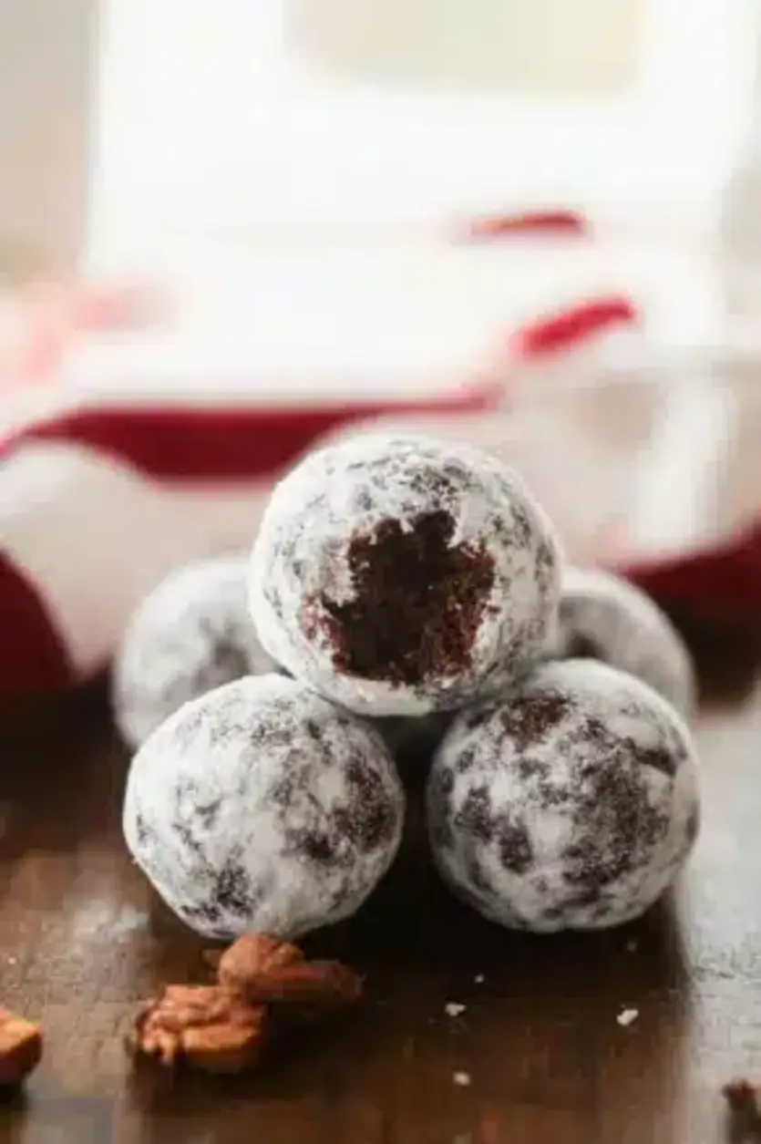A plate of chocolate bourbon balls coated in powdered sugar and chopped nuts