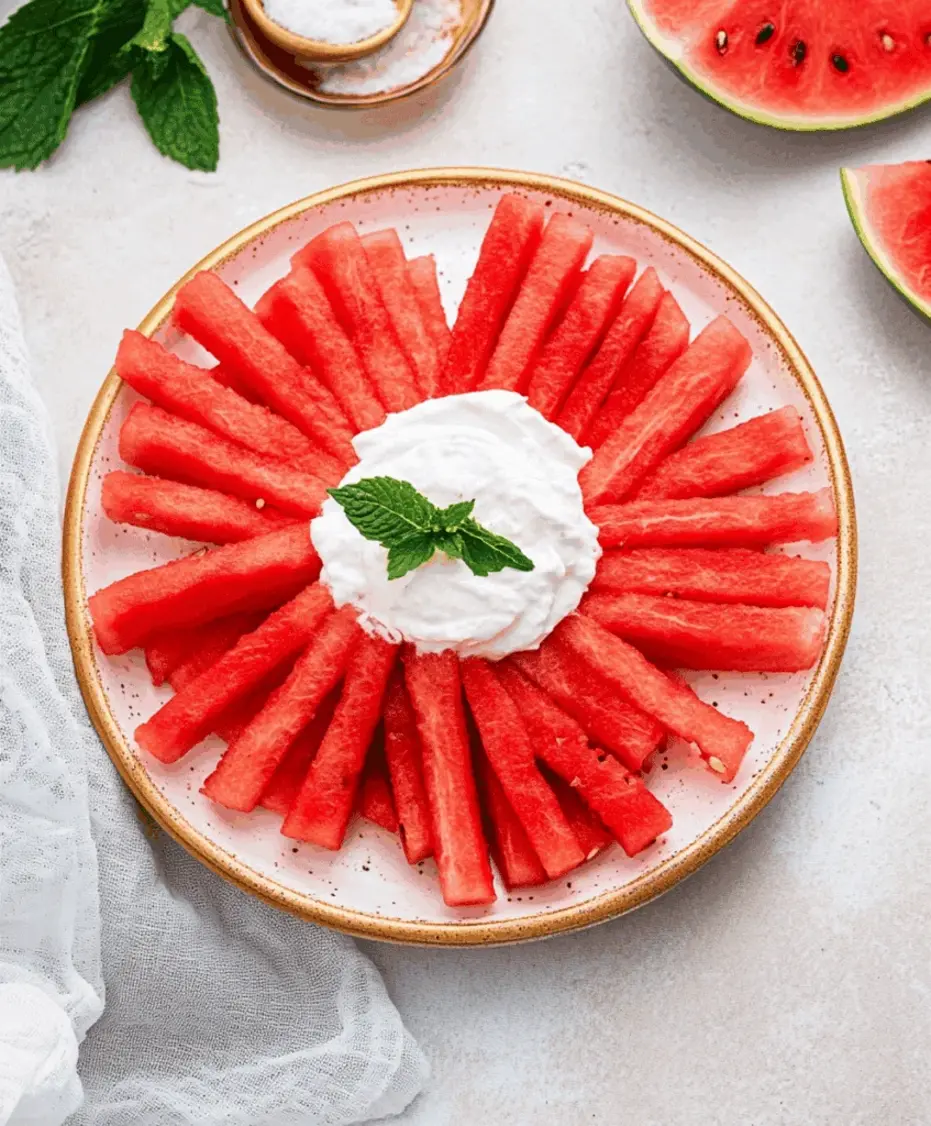 A beautiful presentation of watermelon fries on a rustic wooden board with a bowl of creamy yogurt-lime dip in the center, garnished with lime slices and mint.